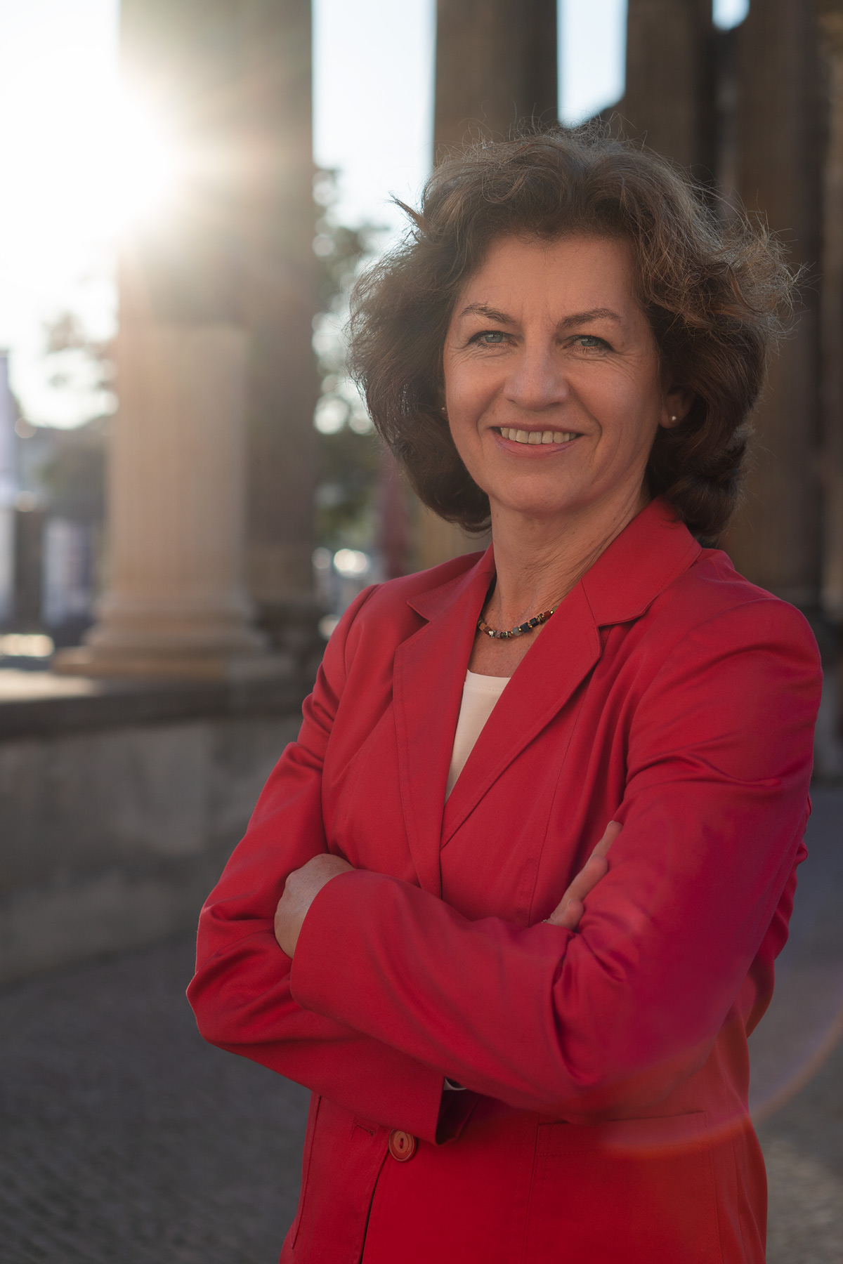 Renate Dahms, stehend, im roten Jacket mit verschränkten Armen, im Hintergrund mehrere Säulen.